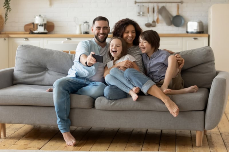 Family of four sitting on the couch together taking photos.
