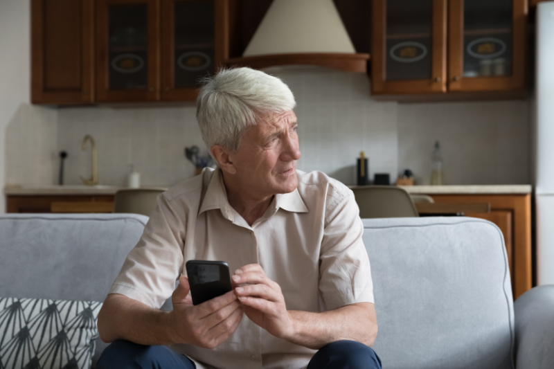 What’s That Smell Coming From My Furnace? Photo of a man looking out a window while sitting on his couch, seemingly concerned.