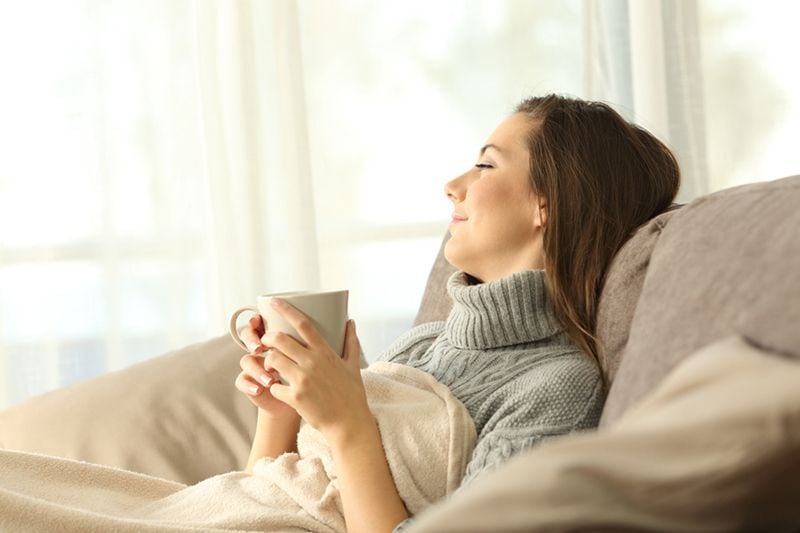 A woman relaxes on a couch with a cup. The Basics of Winter Indoor Air Quality.