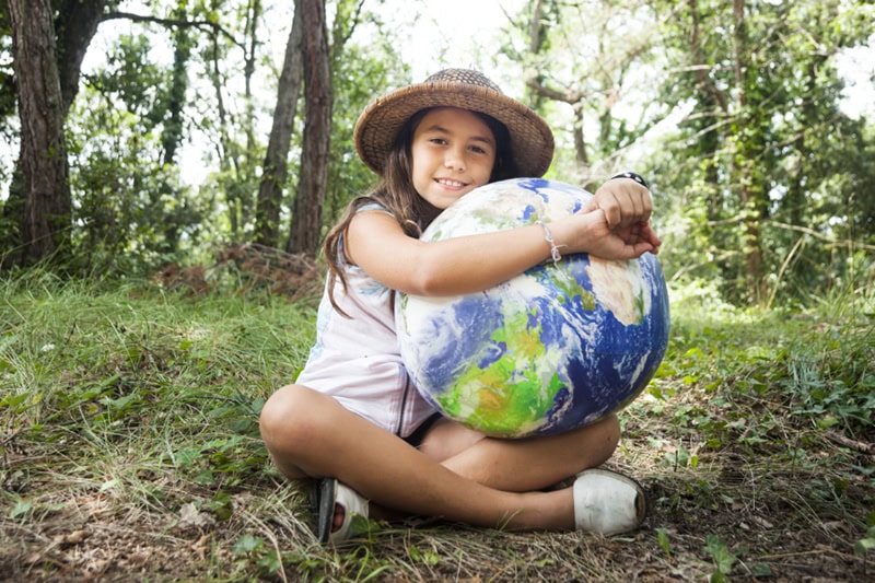 What Does a Geothermal System Cost? Photo of a young girl holding an earth ball, sitting in the woods.